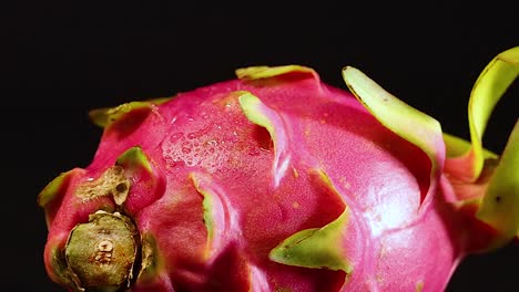 a vibrant dragon fruit being misted, highlighting its pink and green textures against a dark background.