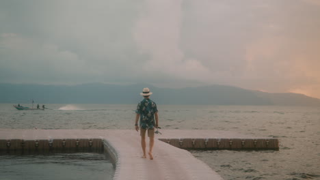 fisherman walking on floating pier in sea with passing boat on background