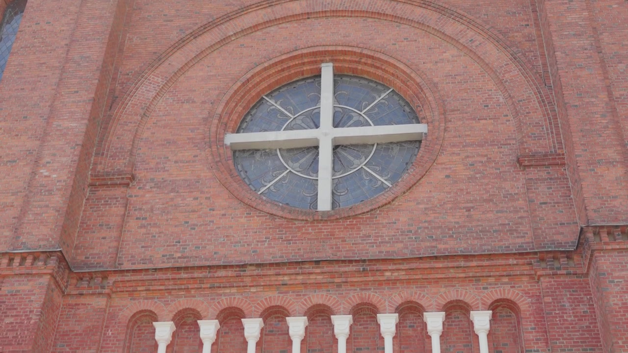 Scatto ravvicinato dettagliato della Chiesa di San Giovanni Battista a Plungė, Lituania, che evidenzia ricche murature in mattoni rossi, colonne bianche e una vetrata sotto una luminosa luce naturale