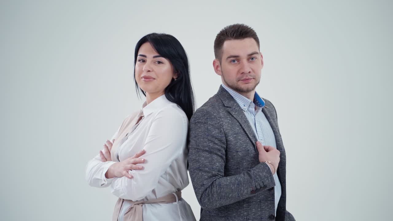 Partners leaning back to back. Young man and woman standing back to back with crossed hands against gray background