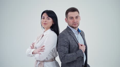 partners leaning back to back. young man and woman standing back to back with crossed hands against gray background