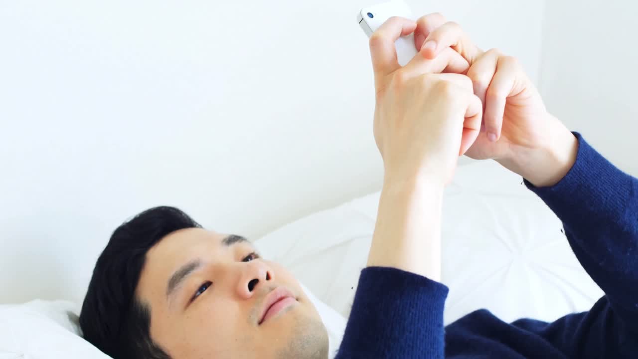 침대 4k에서 휴식을 취하는 동안 휴대 전화를 사용하는 남자