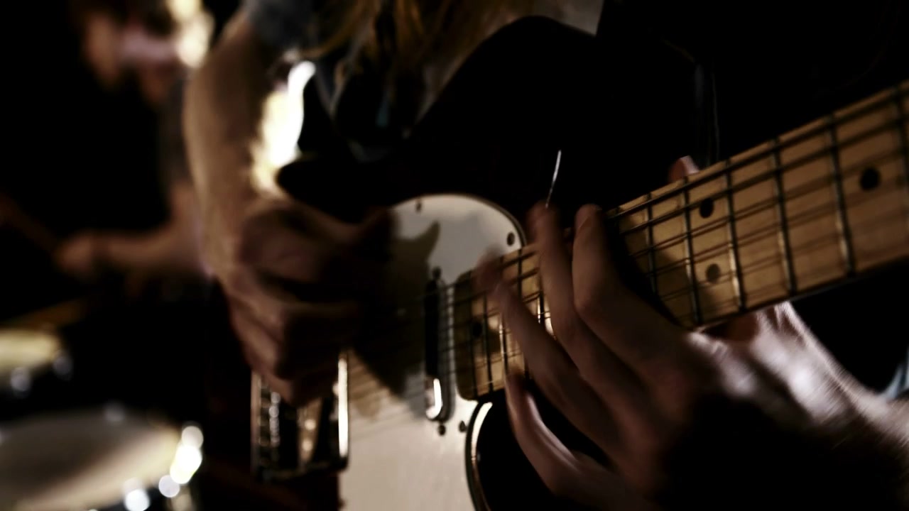 Guitarist spiller på guitarens hals, hvilket skaber lilla markeringer på guitaren, mens trommeslageren rejser sig og slår på bækkenet til en musikreklame