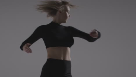 Foto-De-Estudio-De-Una-Joven-Girando-Haciendo-Práctica-De-Baile-Contra-Un-Fondo-Gris