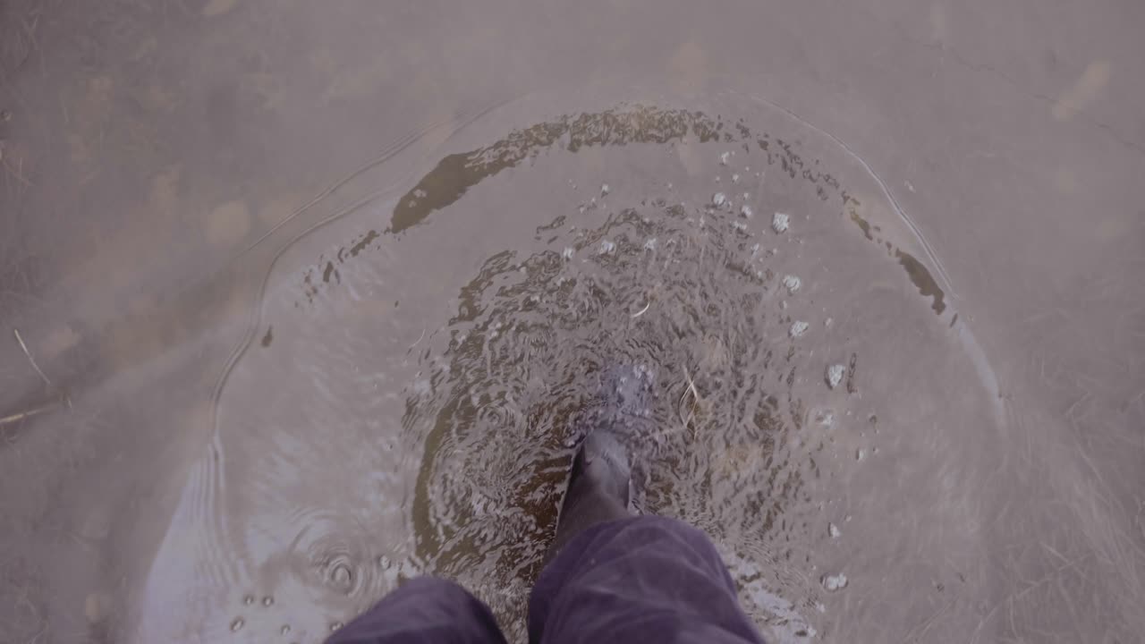 Man in wellies walking in muddy puddles in countryside, slow motion point of view