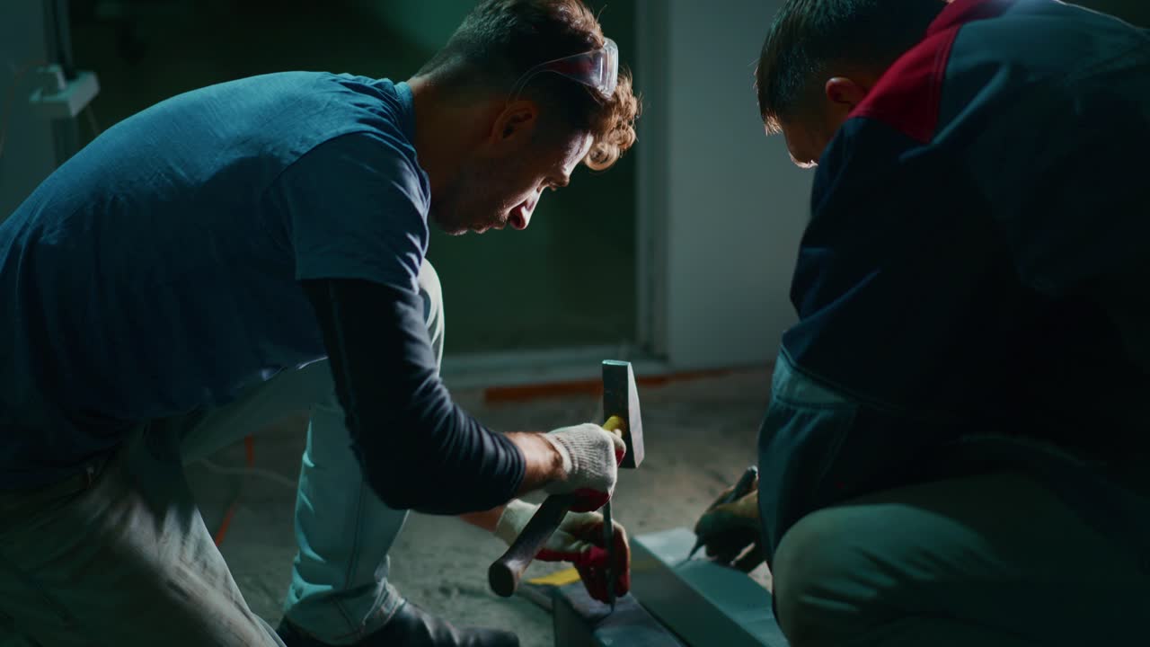 Man Hammering Metal Beam with Chisel in Workshop