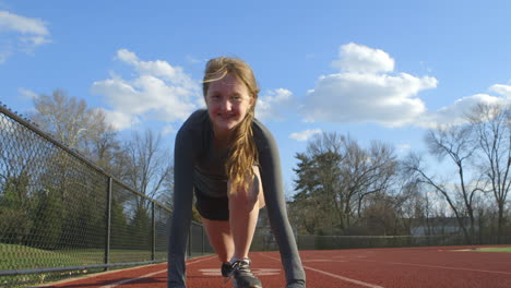 teen girl in the ready position on a track smiles as she looks down the track