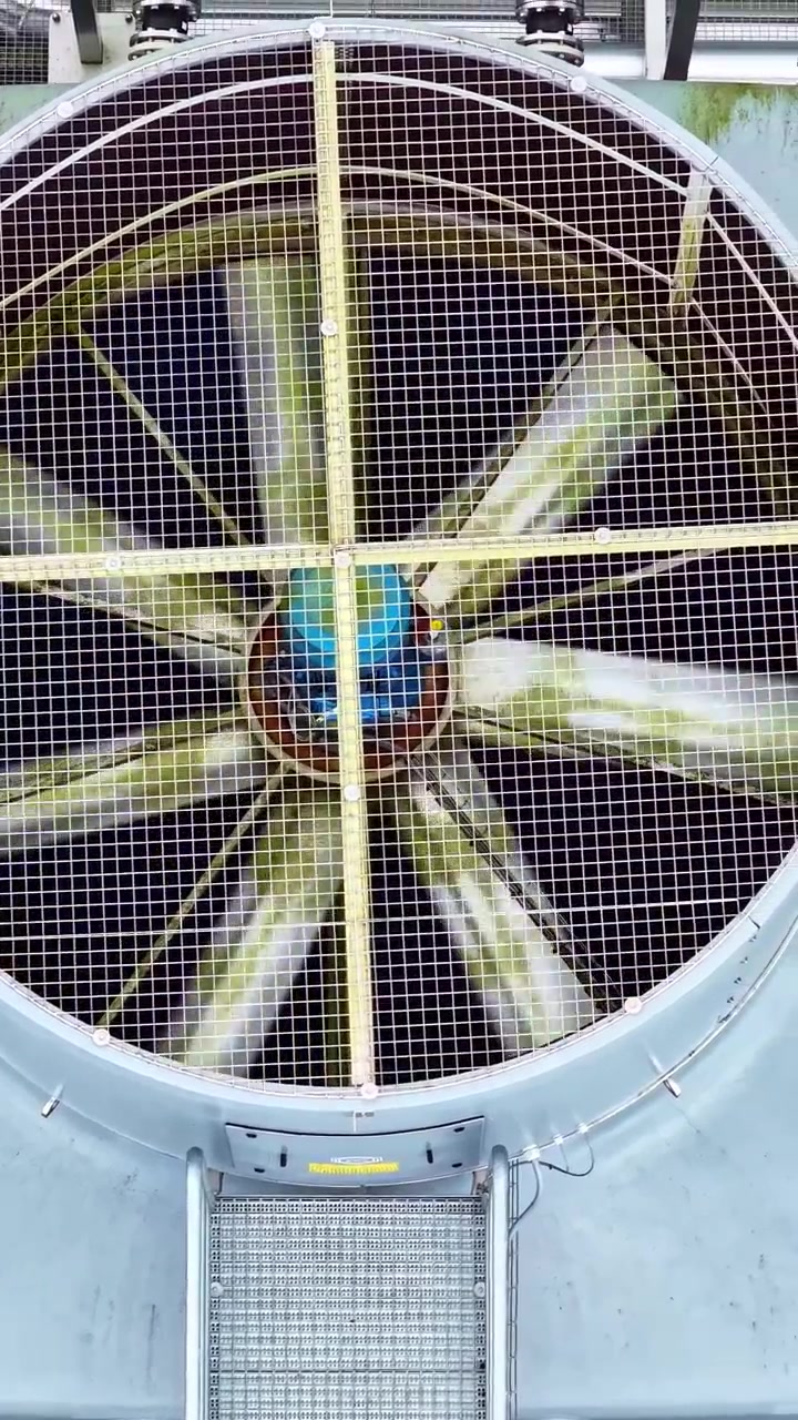 Large industrial ventilation fan spinning behind protective metal safety grid, vertical aerial overview