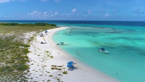 Impresionante-Escena-Aérea-Isla-Tropical-Con-Agua-De-Mar-Turquesa,-Botes-Y-Sombrillas-En-La-Costa-De-Arena-Blanca