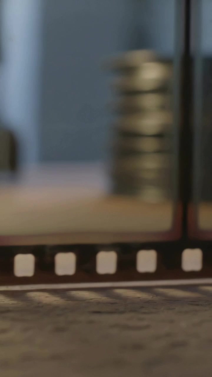 Vertical video: Panning camera revealing film sprocket on textured mat in room with blurred coins