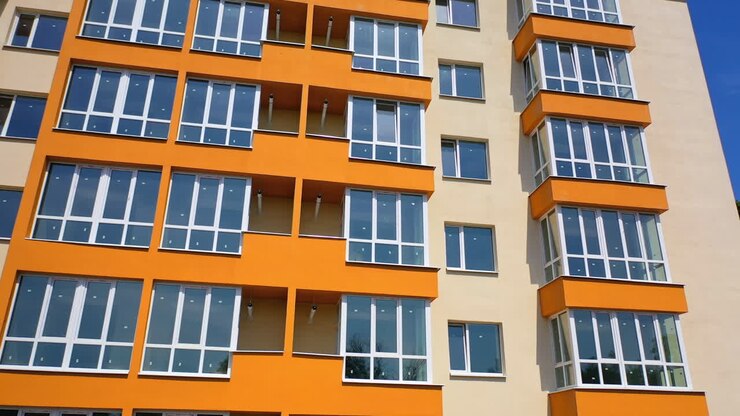Modern high rise building with glazed balconies. Front view of newly built block of flats with colorful walls. New apartment building facade in the city.