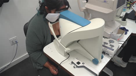 woman checking her eyes through automatic perimeter equipment at optometrist clinic. - closeup shot