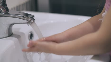 little girl washes hands with water over sink close view