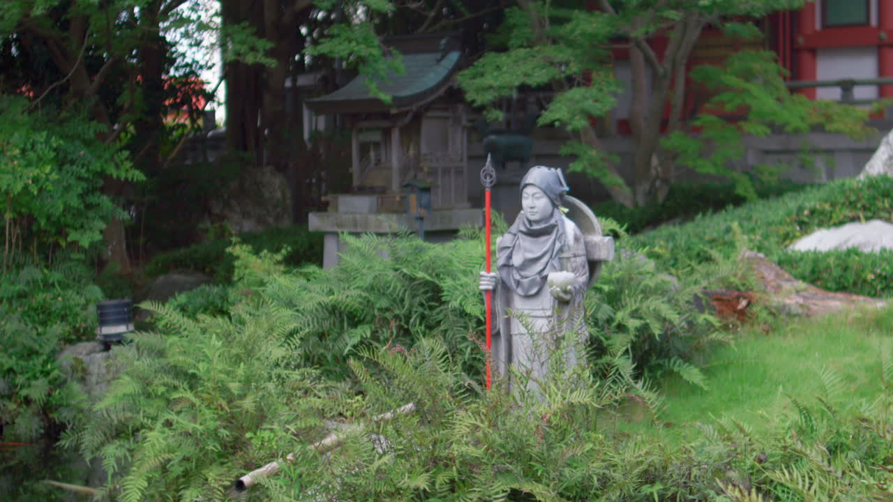 Steinstatue av Jizo Bodhisattva med stav i en frodig japansk buddhistisk tempelhage.