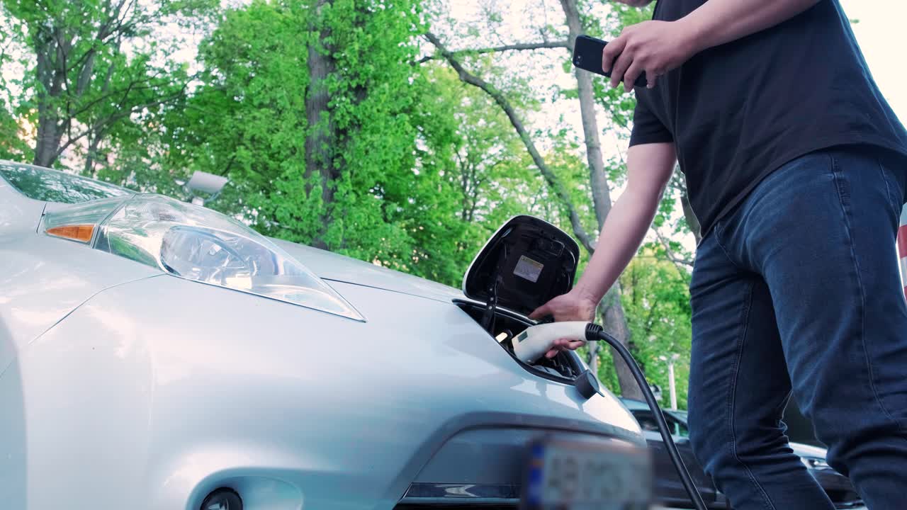 전기 자동차의 연료 충전 과정: 전기 에코 자동차가 충전하는 치 아래의. 전기 자동차 충전 치는 자동으로 열립니다. 남성 손이 발기 된 자동차를 입합니다.