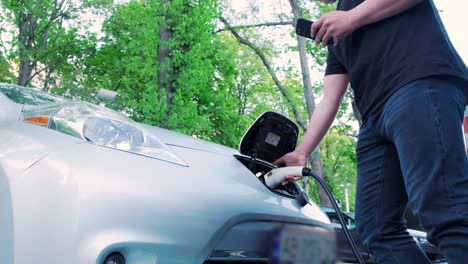 proceso de reabastecimiento de combustible de un automóvil eléctrico. un disparo debajo de la escotilla donde se carga el automóvil ecológico eléctrico. la escotella de carga del automóvil eléctrico se abre automáticamente. una mano masculina inserta un automóvil erecto