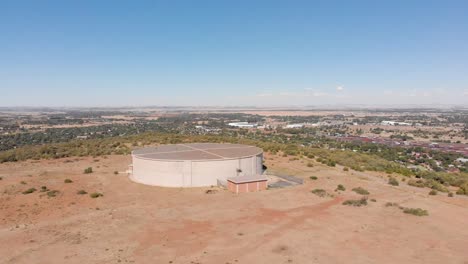 DRONE-Shot-of-Water-Supply-Tank-supplying-water-to-a-Town-in-the-Background-on-a-Sunny-Day
