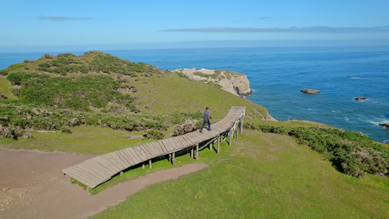 Bird's eye view of a young man walking up the pier of souls in Cucao in Chiloe Chile, alone meditating