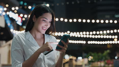 Woman using mobile phone and credit card for online shopping at night