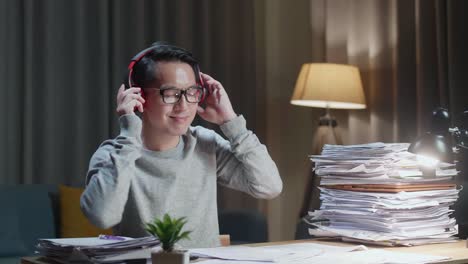 asian man wearing headphones and listening to music after working with documents at home