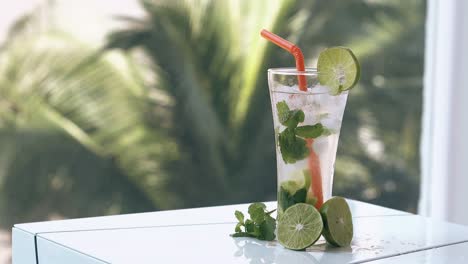 fresh lime halves and small mint leaves lie near tall glass