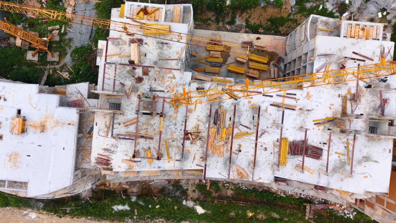 Vista aérea cenital de los pisos de hormigón de un edificio en construcción. Toma de dron cenital que muestra losas de hormigón, andamios y el brazo de una grúa torre en una obra.