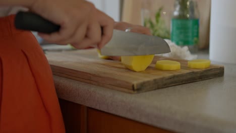 close up of a woman slicing potatoes with a chef knife in a small kitchen with natural light