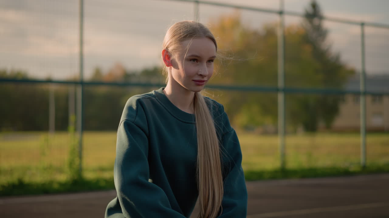 primer plano de una mujer realizando un ejercicio de fitness mientras se arrodilla hacia adelante, su cabello fluye por el pecho contra un fondo brillante con un árbol y un edificio en la distancia