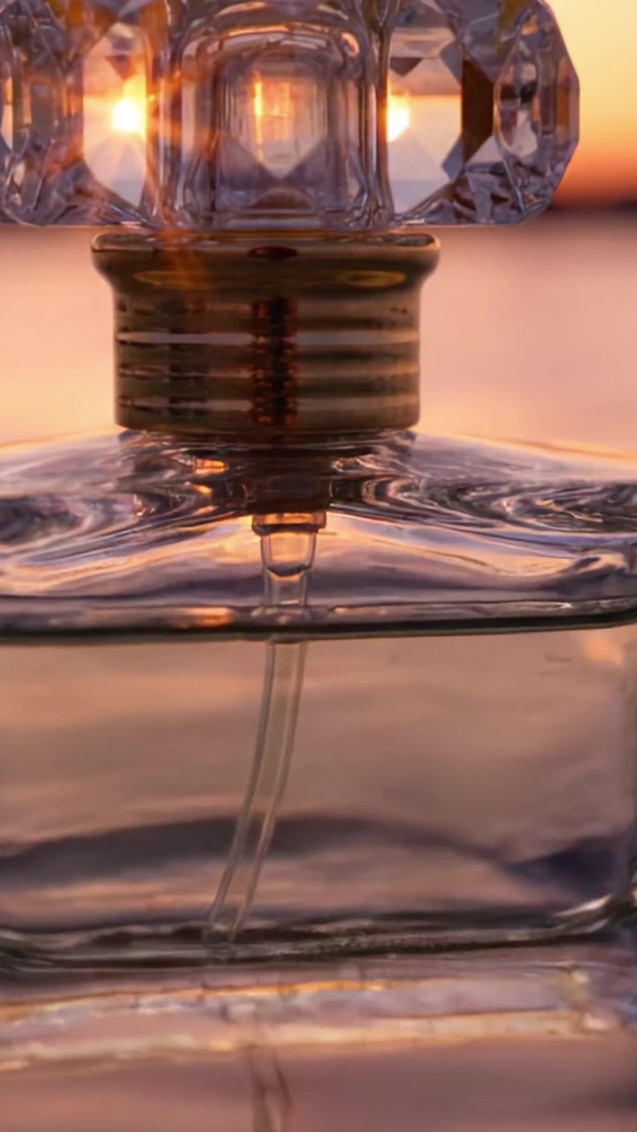 Un primo piano di una lussuosa bottiglia di profumo che cattura il luccichio dei riflessi del tramonto nel suo vetro e un sentore della fragranza al suo interno.