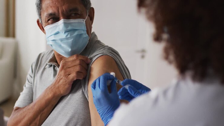 Mixed race female doctor wearing mask giving vaccination to senior man at home