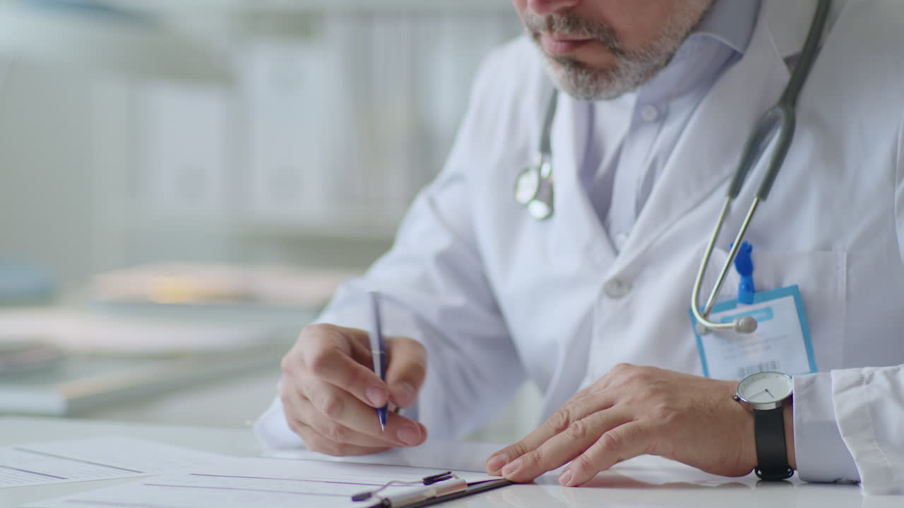 Male Doctor Filling Out Documentation Form at Desk in Clinic