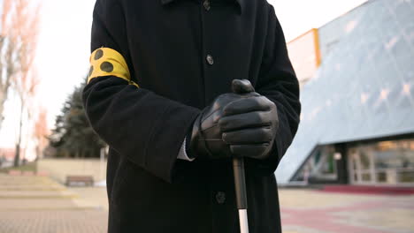 close up of an unrecognizable blind man in coat and gloves holding walking stick while standing in the street on a winter day