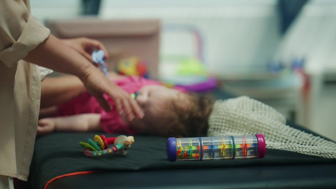Bebê deitado em um trocador enquanto um adulto oferece gentilmente uma chupeta e brinquedos, criando uma cena calma de cuidado infantil diário