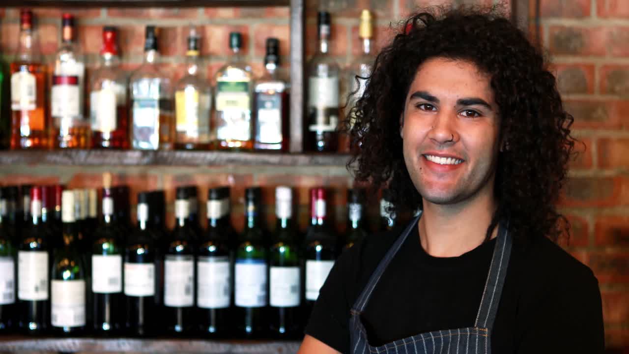 Ritratto di barman in piedi con le braccia incrociate al bancone del bar
