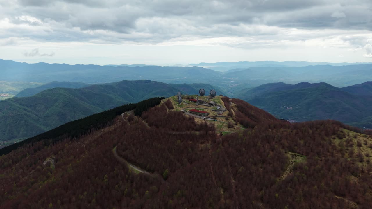 Old military radar site on mountain top under cloudy sky, wide aerial scenic view