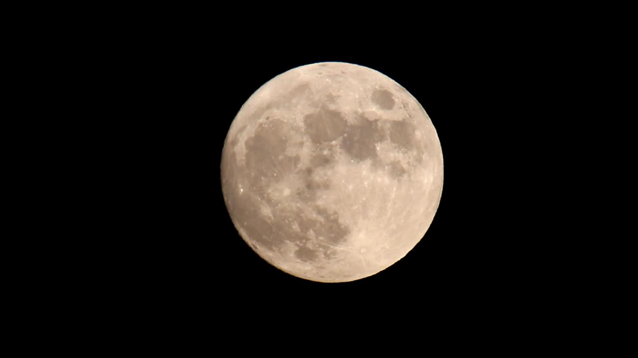 Lua cheia laranja e amarela brilhante contra um céu preto escuro, movendo-se do centro do quadro diagonalmente para o canto superior direito.