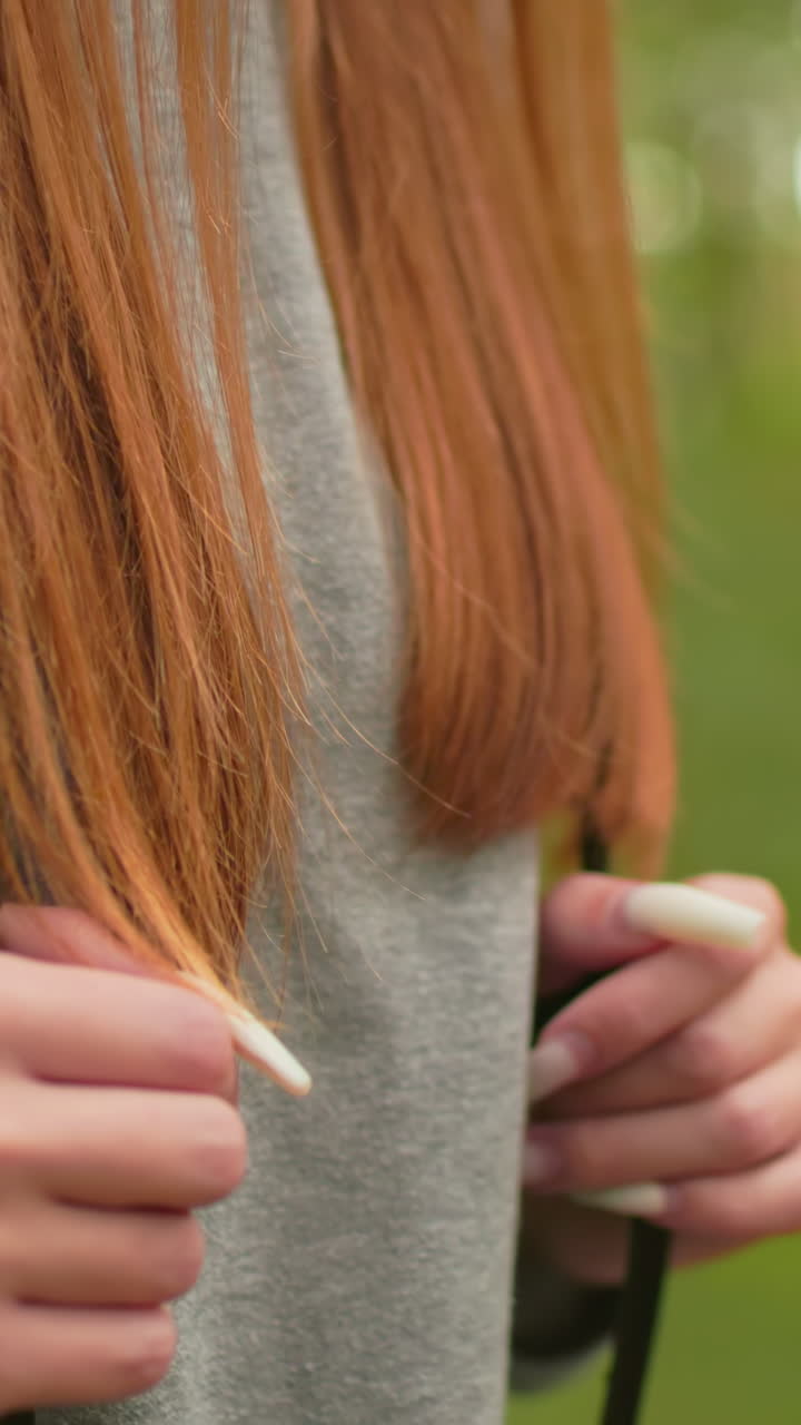 primer plano de una mujer caminando a través de un bosque exuberante, agarrando correas de mochila con uñas largas y cabello largo que fluye sobre los hombros, usando una sudadera gris y una expresión enfocada