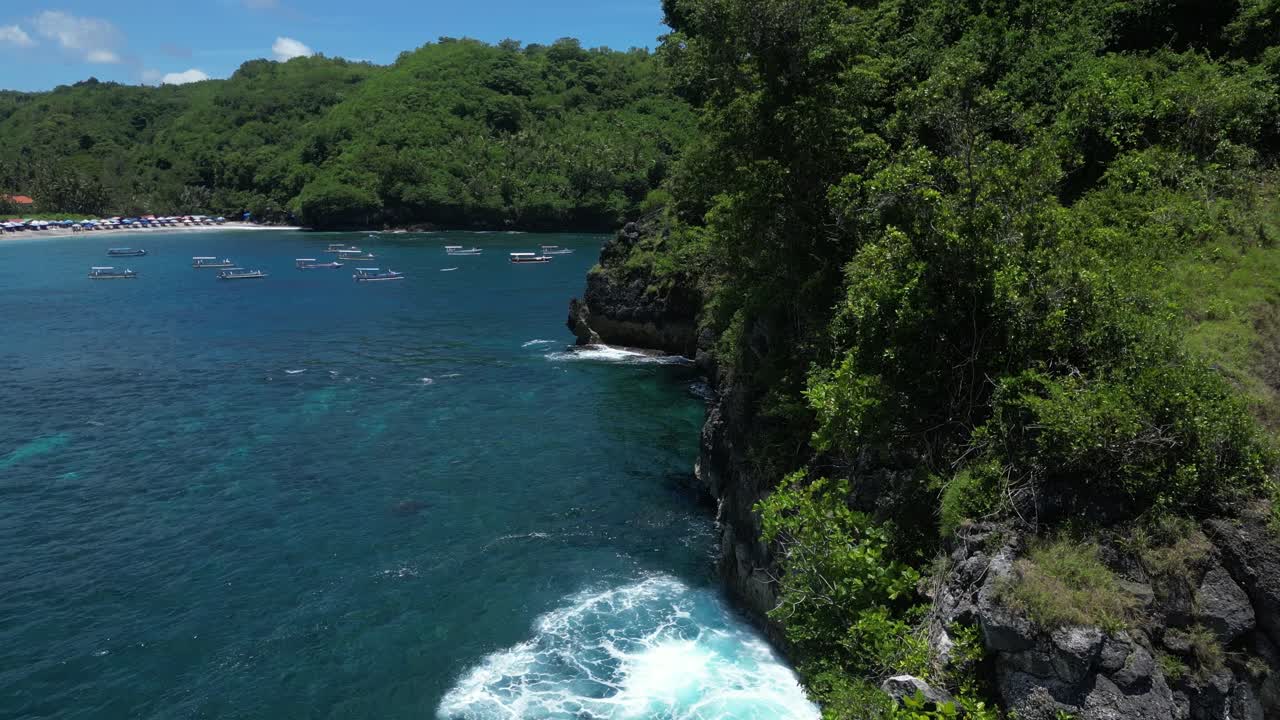 A lonely island off the coast of Nusa Penida with a rocky arch and greenery with blue crashing waves, aerial