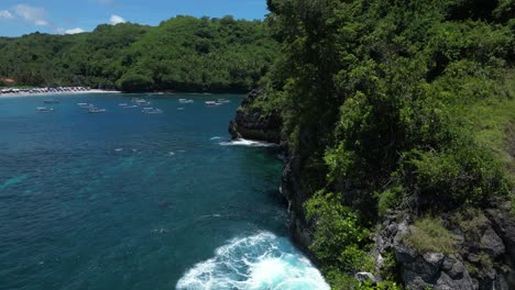 una isla solitaria en la costa de nusa penida con un arco rocoso y vegetación con olas azules que se estrellan, aérea