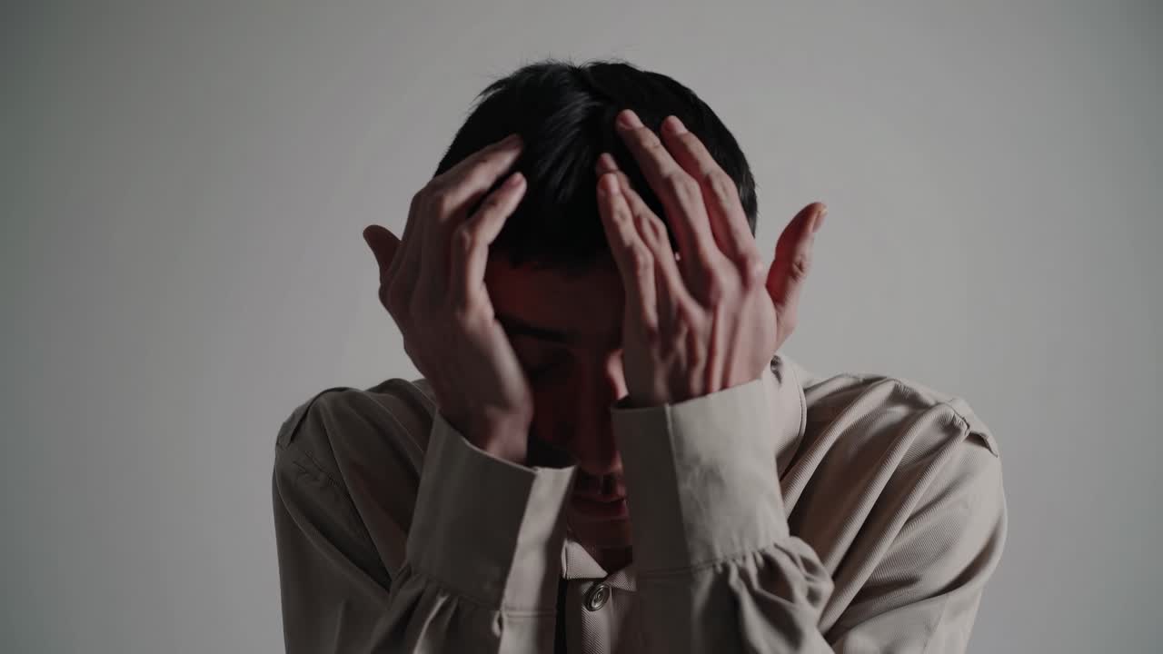 Artistic video still of a person in a beige shirt covering their face with hands