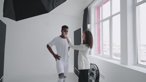 detrás de las escenas de una sesión de fotos: una hermosa modelo negra jugadora de fútbol se está preparando para una sesión de fotos para una revista un artista de maquillaje corrige el tono de la piel para fotos en una revista deportiva