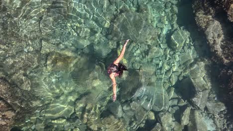 a petite pool, surrounded by volcanic rocks along the ocean, is the serene setting for a swimsuit-clad model to unwind