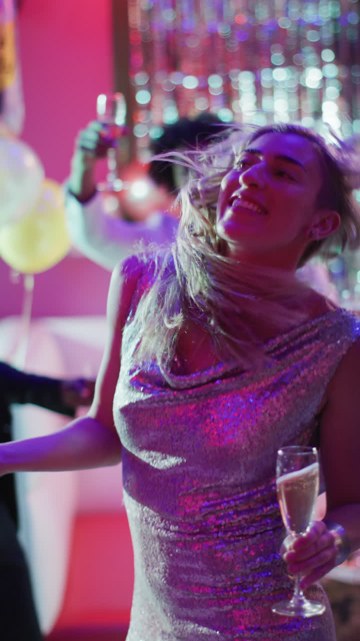 Vertical video of happy caucasian woman dancing holding a champagne glass at a nightclub