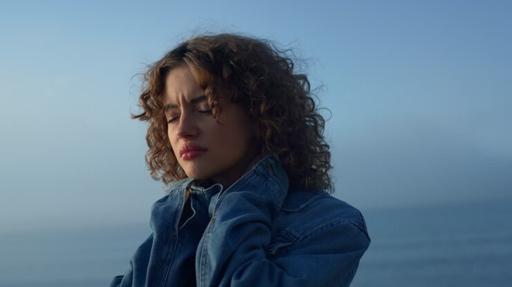 Sad girl standing on ocean beach. Distressed woman touching neck with hands