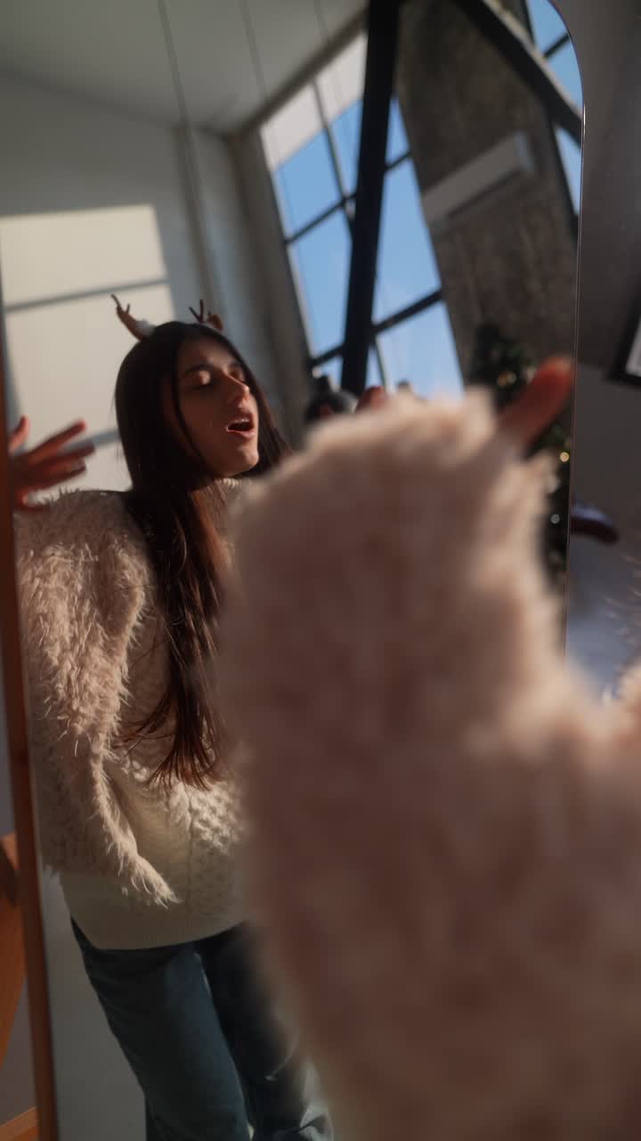 Donna con un maglione comodo che si guarda allo specchio vicino a un albero di Natale