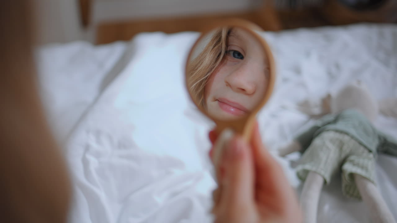 Curious kid mirror reflection in bedroom closeup. Smiling girl looking herself