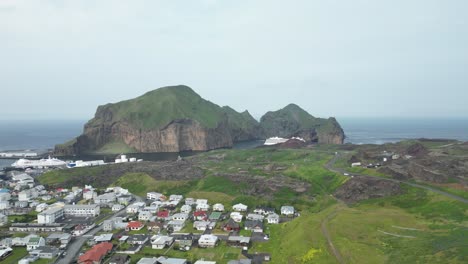 Aerial-drone-shot-of-the-town-of-Westman-Island,-looking-over-the-harbor,-cruise-ships-and-old-lava-fields