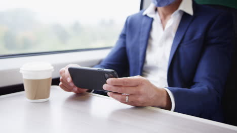 Close-Up-Of-Businessman-On-Train-Using-Mobile-Phone-Wearing-PPE-Face-Mask-During-Health-Pandemic