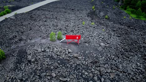 Große-Rote-Bank,-Eingebettet-In-Eine-Landschaft-Aus-Grauem-Vulkangestein-Mit-Vegetation-Aus-Einigen-Grünen-Pflanzen