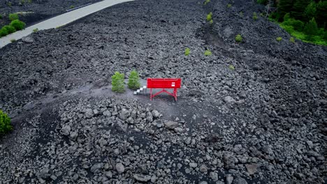 large red bench inserted in a landscape of gray volcanic rocks with vegetation of a few green plants